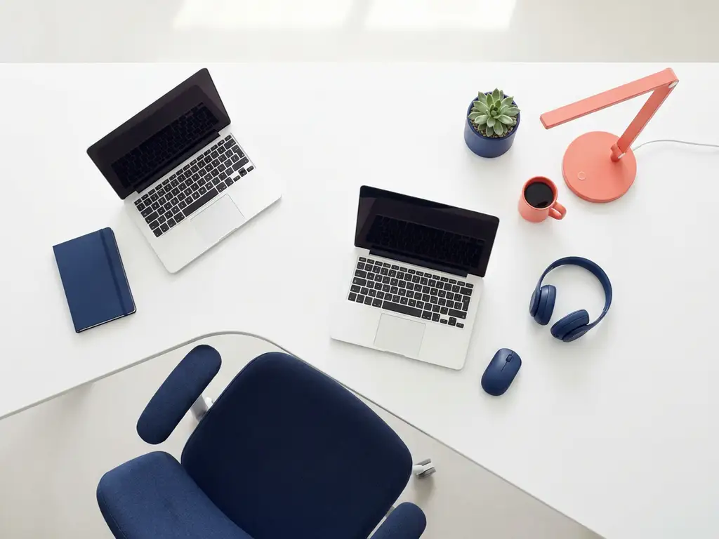 Moderne werkplek met laptop, ergonomische stoel, bureaulamp, plant en kantoorbenodigdheden in navy en koraal tinten