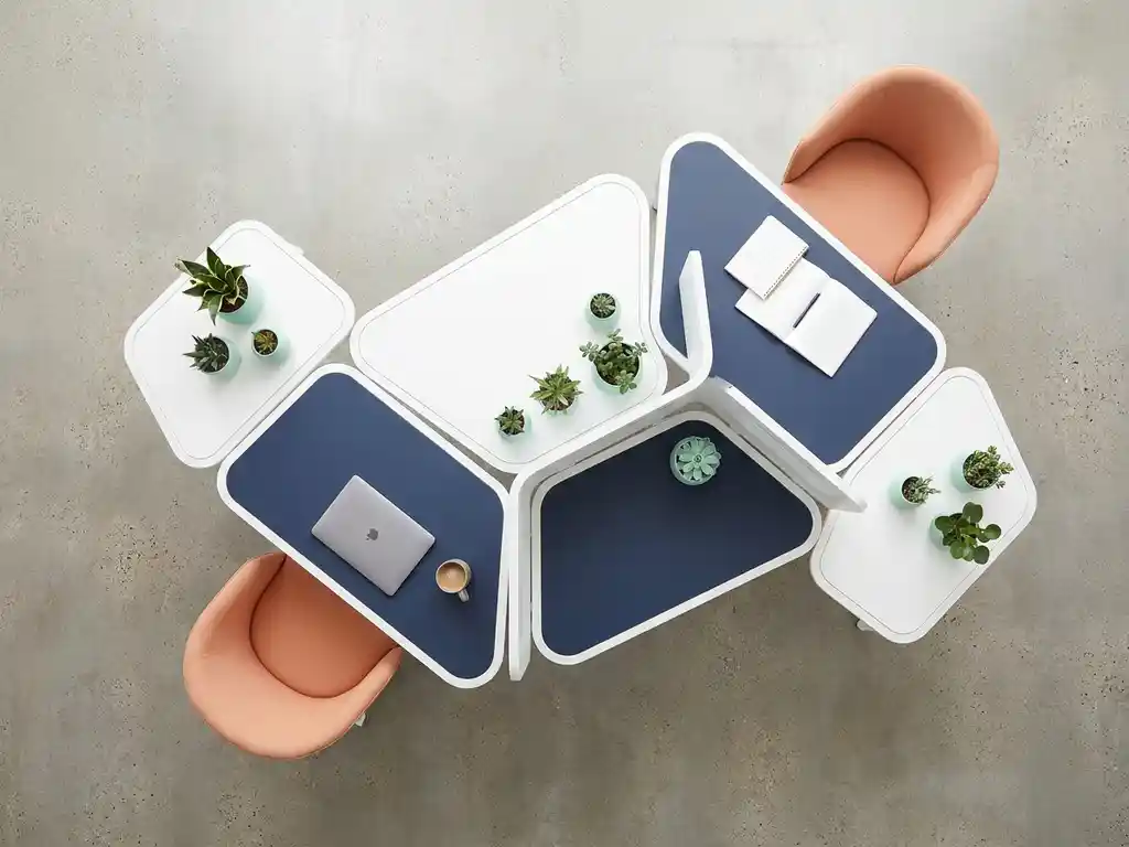Modulair wit bureausysteem met geometrische secties die uitbreiden als puzzelstukken, laptop en planten op marineblauwe oppervlakken met perzikkleurige stoelen